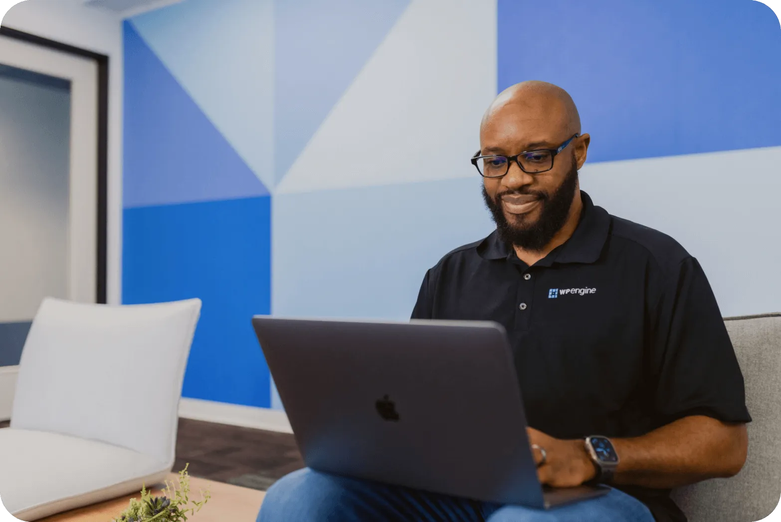 smiling man with laptop in front of geometric accent wall