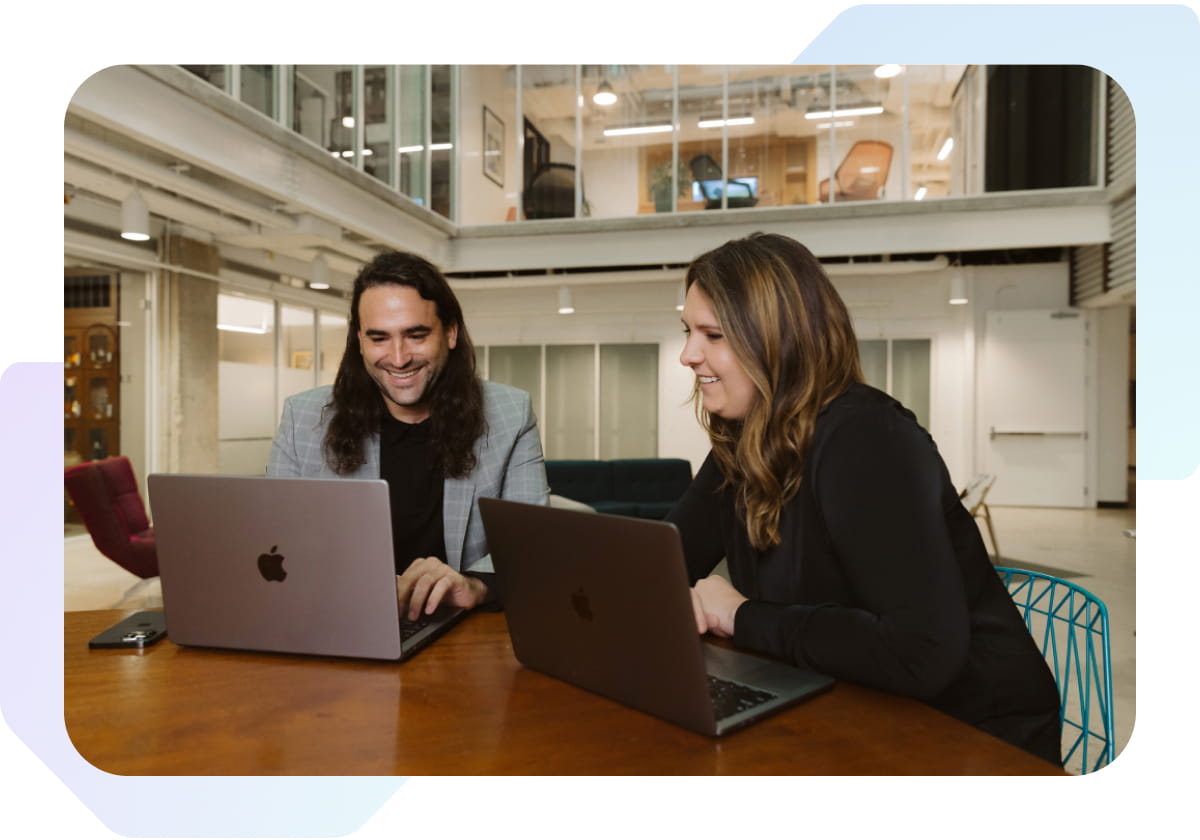 Man and woman sitting at a desk looking at laptops and smiling