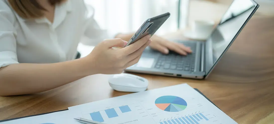 Person using laptop and phone with printed chart graphs